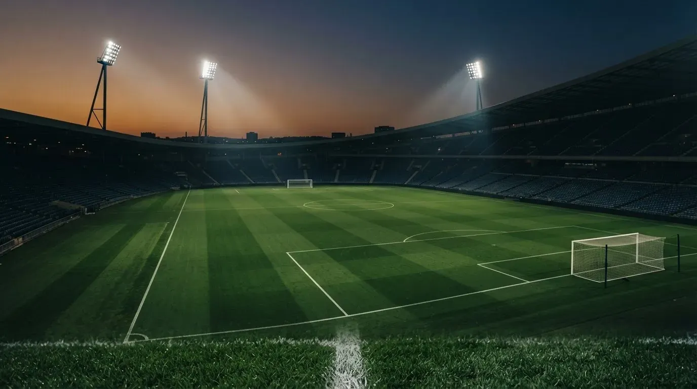 An empty football stadium with floodlight masts at dusk