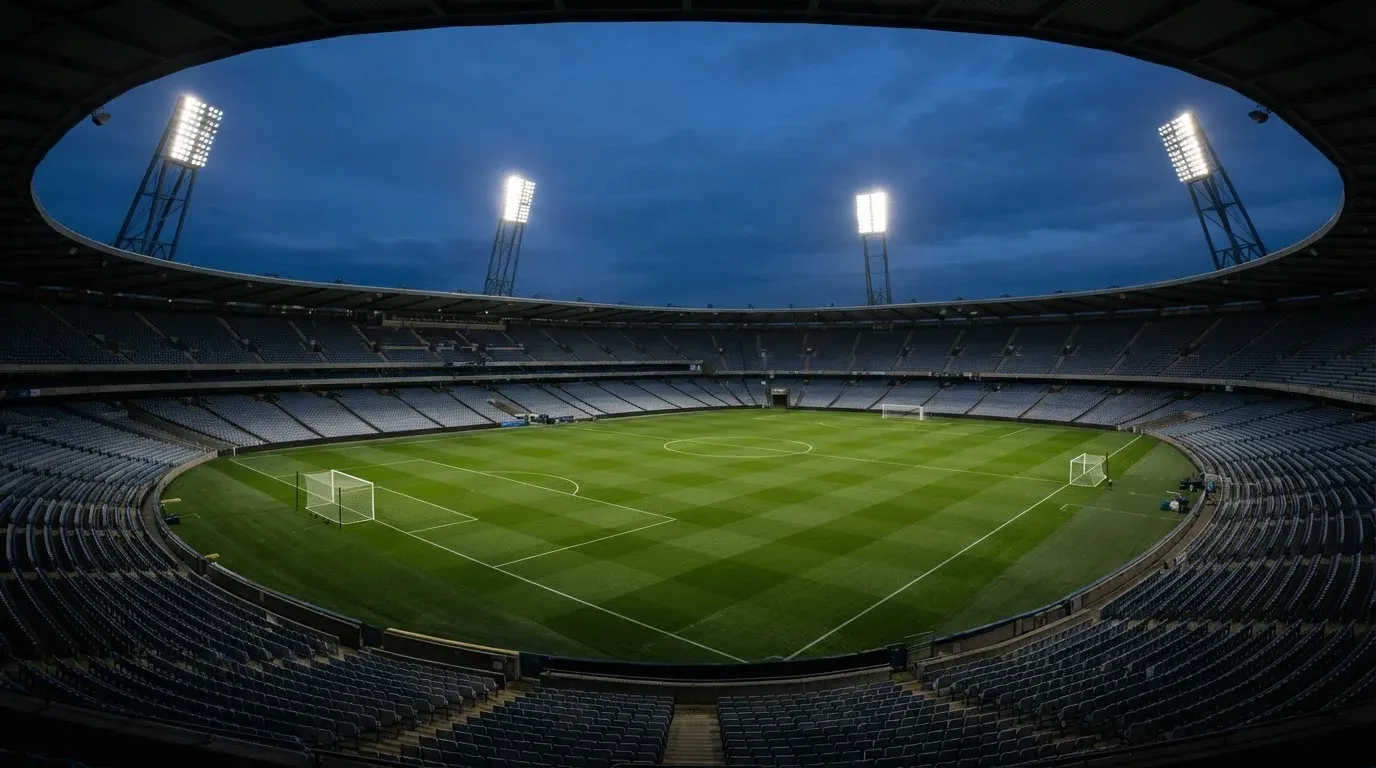 An empty football stadium with floodlight masts at dusk