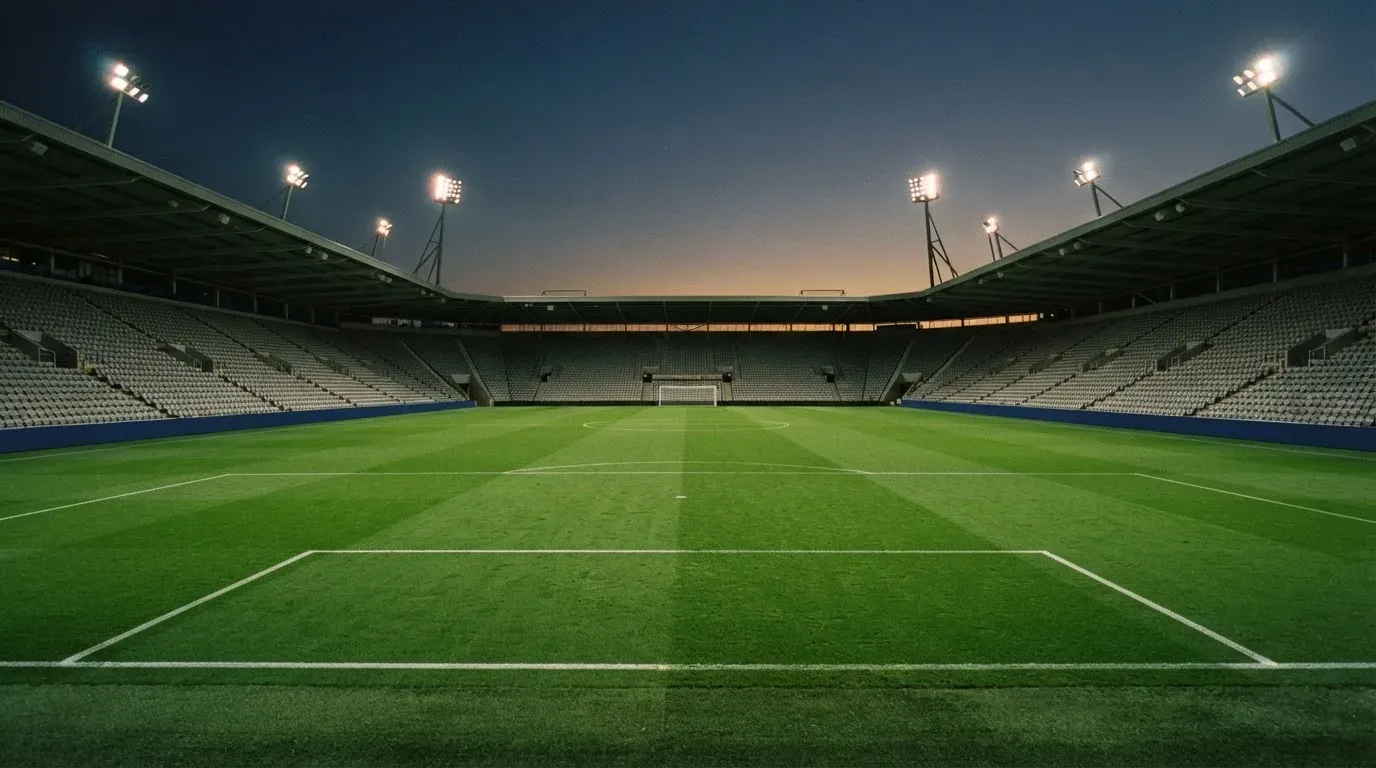 An empty football stadium with floodlight masts at dusk