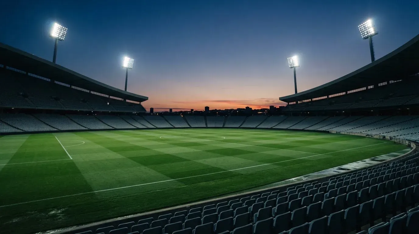 An empty football stadium with floodlight masts at dusk