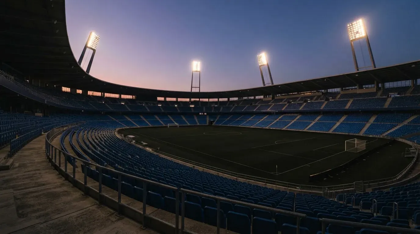 An empty football stadium with floodlight masts at dusk