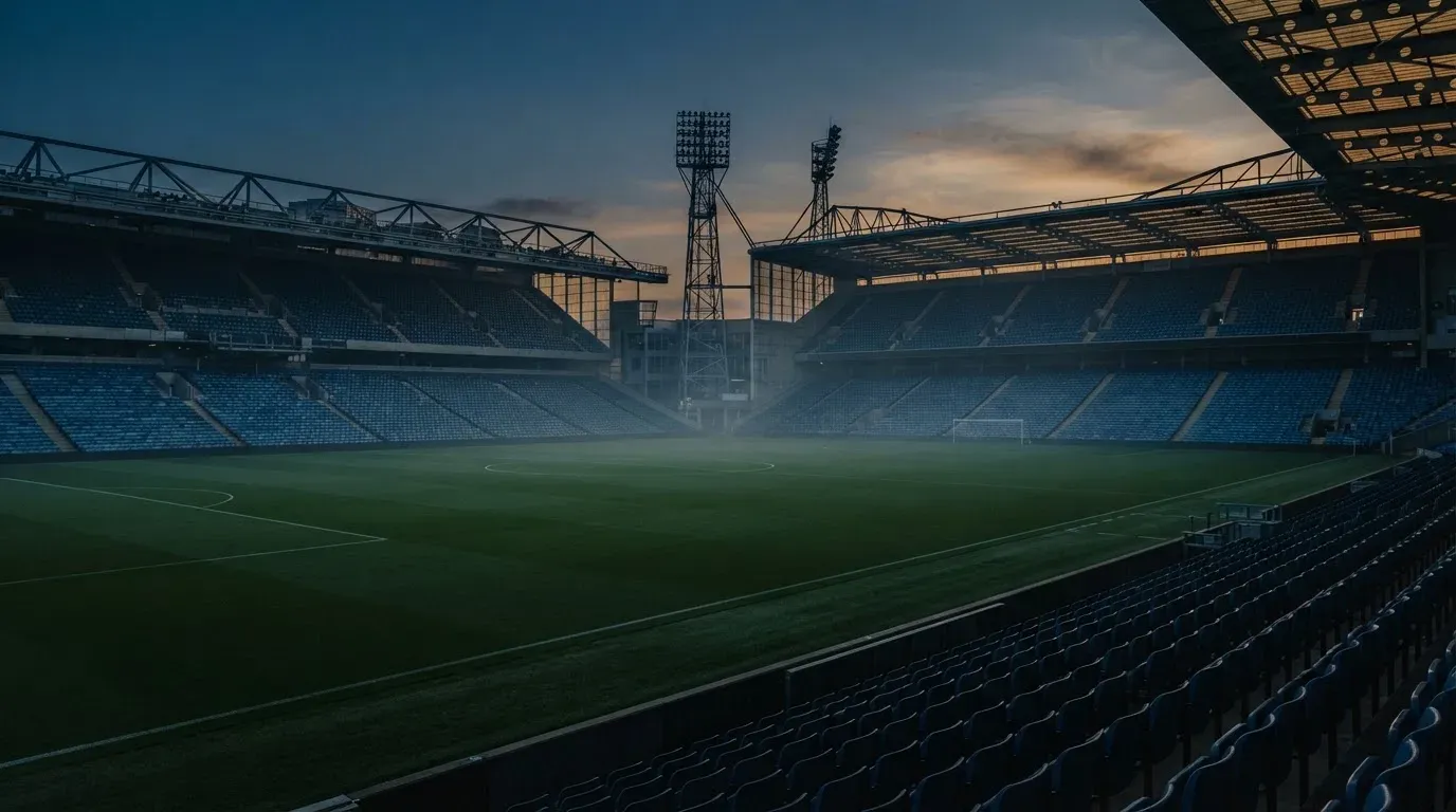 An empty football stadium with floodlight masts at dusk