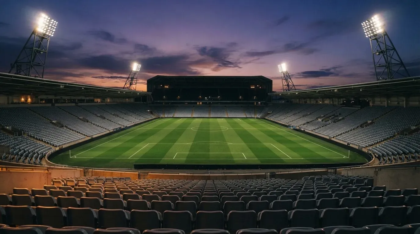 An empty football stadium with floodlight masts at dusk