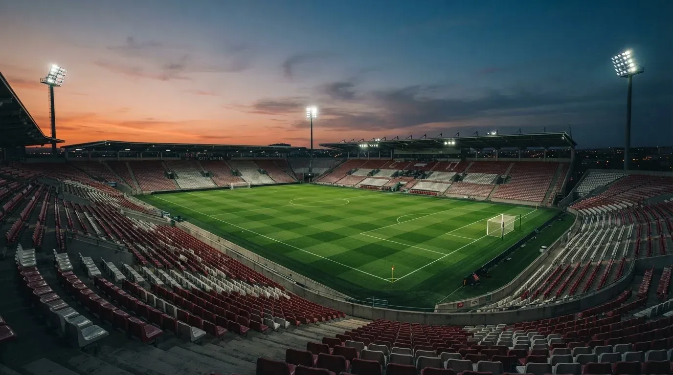 An empty football stadium with floodlight masts at dusk