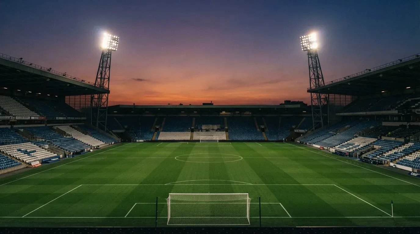 An empty football stadium with floodlight masts at dusk