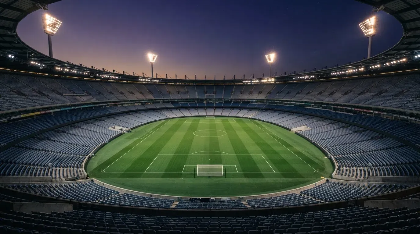 An empty football stadium with floodlight masts at dusk